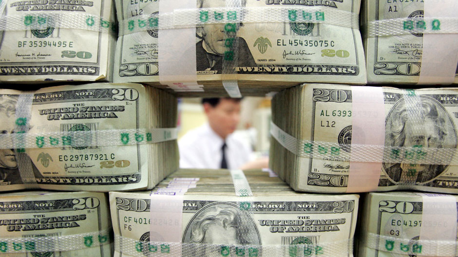 A bank clerk works behind twenty-dollar bills piled at a bank in Seoul November 9, 2004