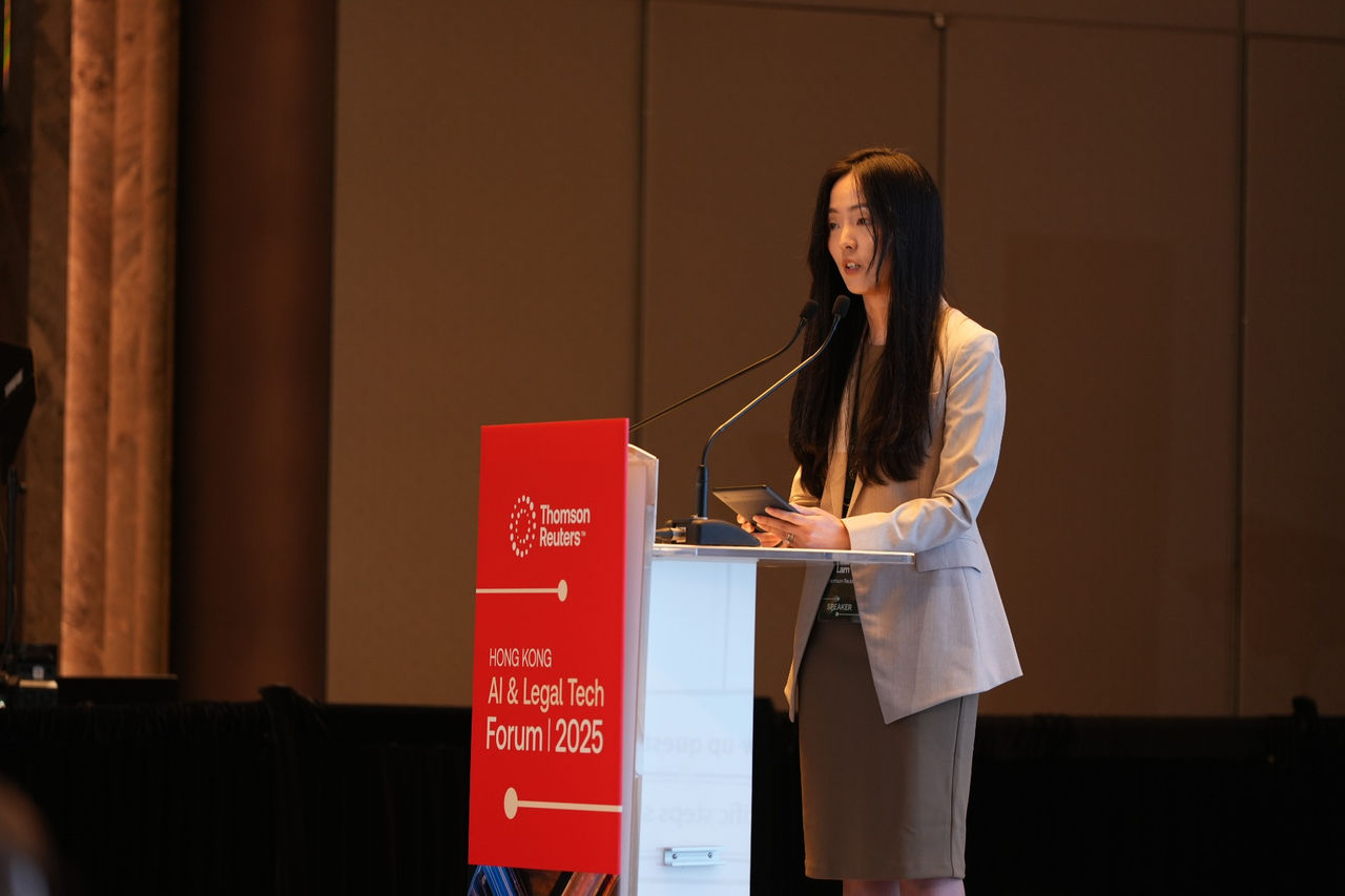 Presenter standing at a podium delivering remarks at the Hong Kong AI & Legal Tech Forum 2025.